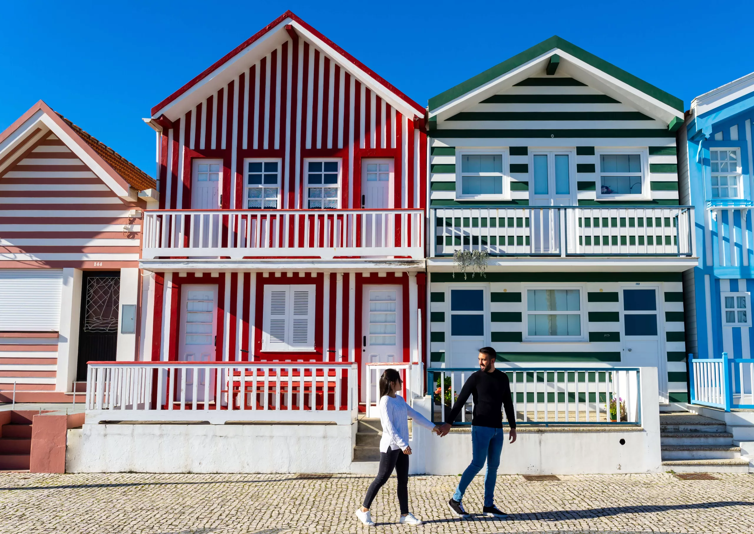 woman-and-man-strolling-on-a-sightseeing-tour-of-the-colorful-houses-of-costa-nova-in-portugal